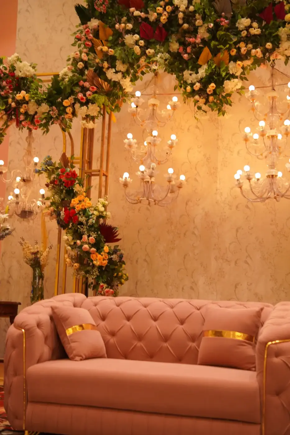 Blush tufted couch beneath floral installations and chandeliers