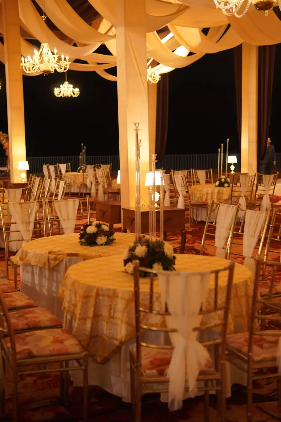 Draped open-air dinner setup lit by chandeliers at night